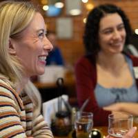 Two event guests, sitting at table and smiling at something off camera